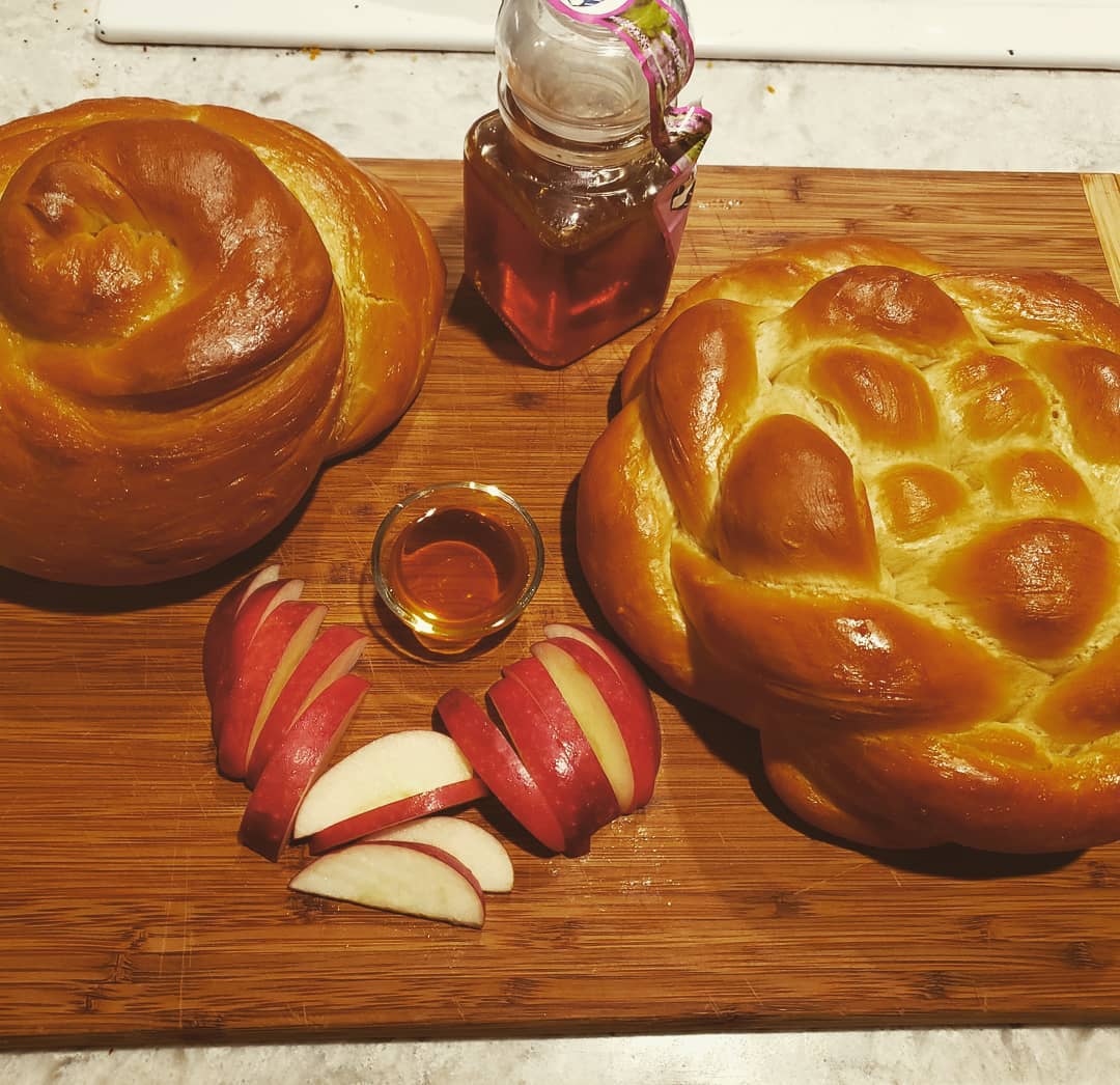 A cutting board with Rosh Hashanah challah bread, apples, and honey